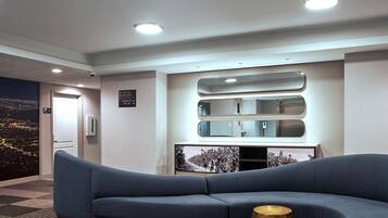 A modern living room with a blue sofa, a decorative mirror, and a cityscape mural on the wall.
