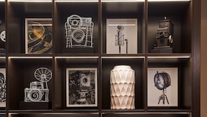 A dark wooden shelving unit with various framed photographs and decorative items, including a white vase and two wicker baskets filled with oranges. - Hampton Inn & Suites Los Angeles/Sherman Oaks (Van Nuys)
