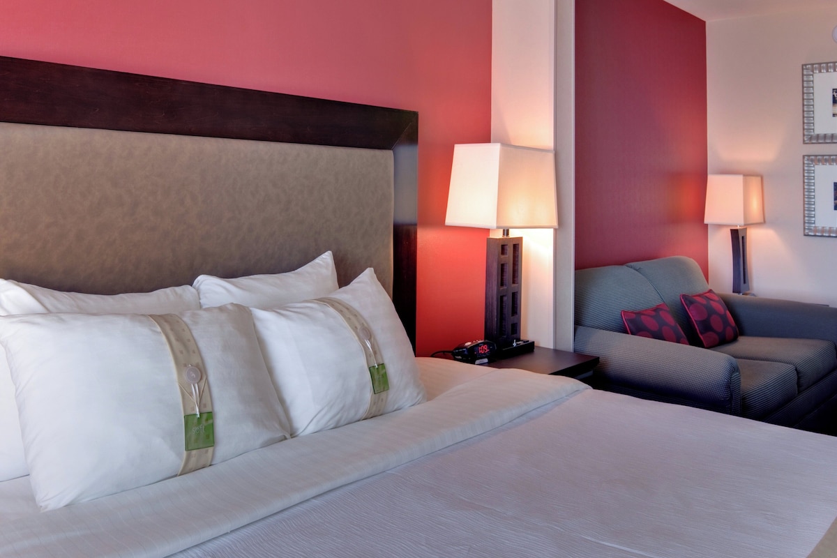 Habitación de hotel con cama, dos mesitas de noche, sofá y dos lámparas de pared.