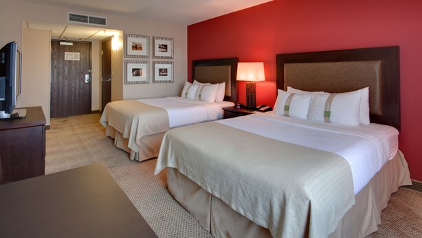 A hotel room with two beds, a desk, a TV, and a red accent wall. - Holiday Inn & Suites Bakersfield by IHG (Bakersfield)