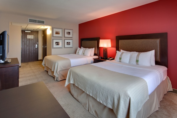 Habitación de hotel con dos camas, un escritorio, un televisor y una pared de acento roja.