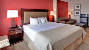 A hotel room with a large bed, two bedside tables with lamps, a small sofa, a desk, and a refrigerator. - Holiday Inn & Suites Bakersfield by IHG (Bakersfield)