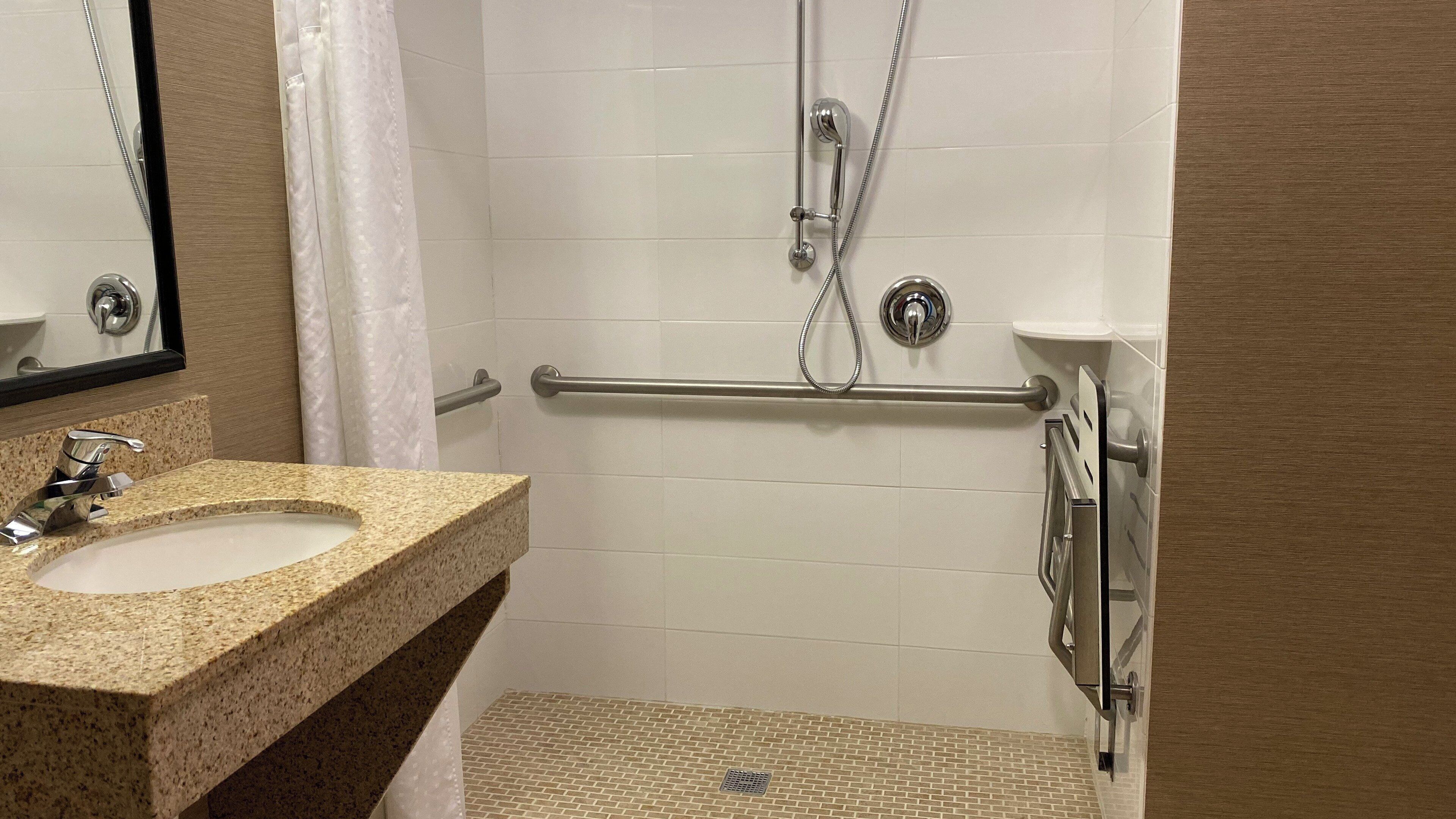 A bathroom with a granite countertop sink, a shower with a grab bar, and a tiled floor.