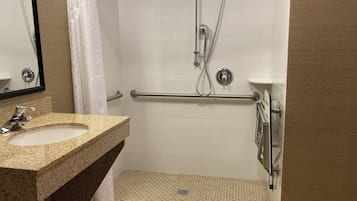 A bathroom with a granite countertop sink, a shower with a grab bar, and a tiled floor.