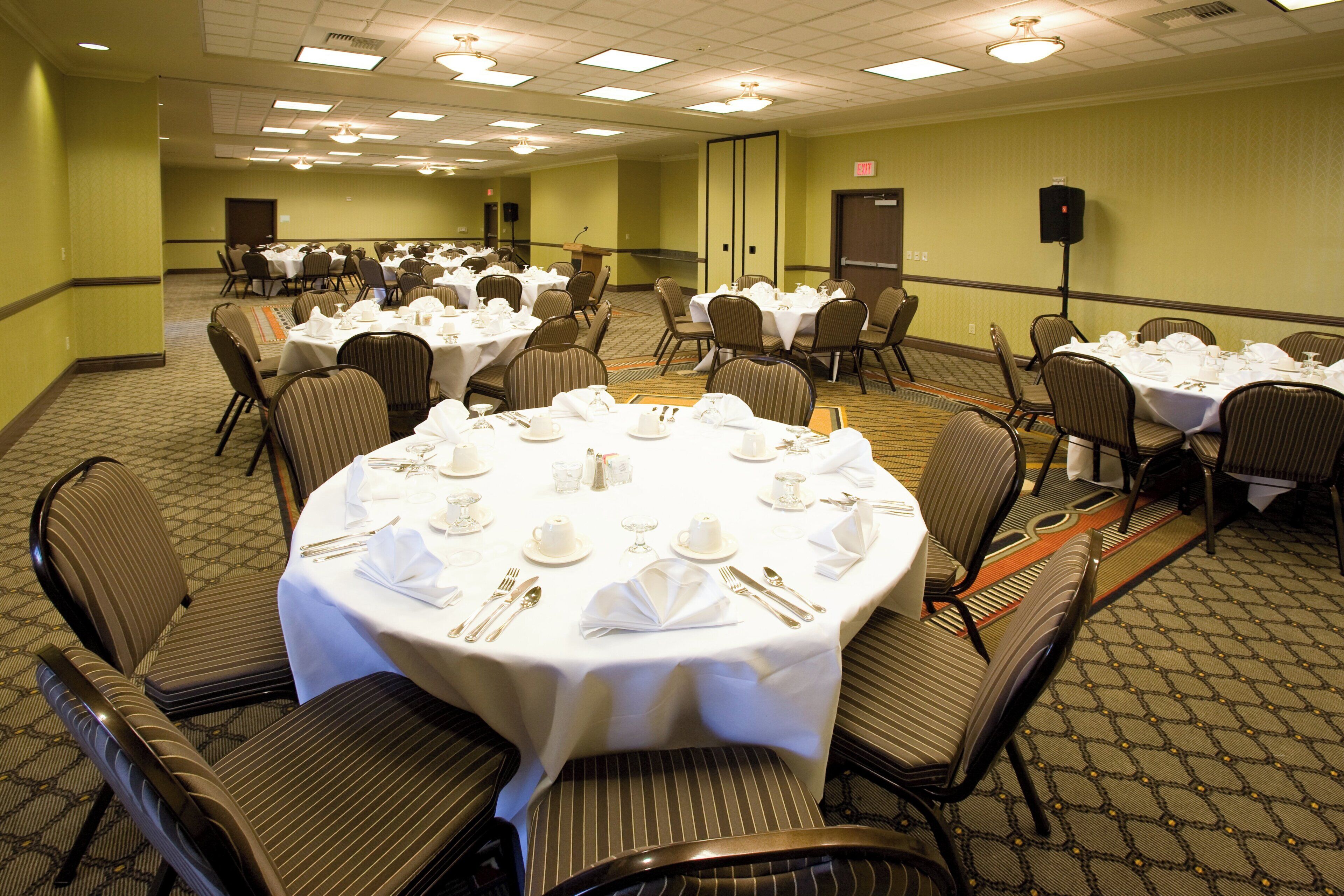 A conference room with multiple round tables set for dining, equipped with chairs and table settings.