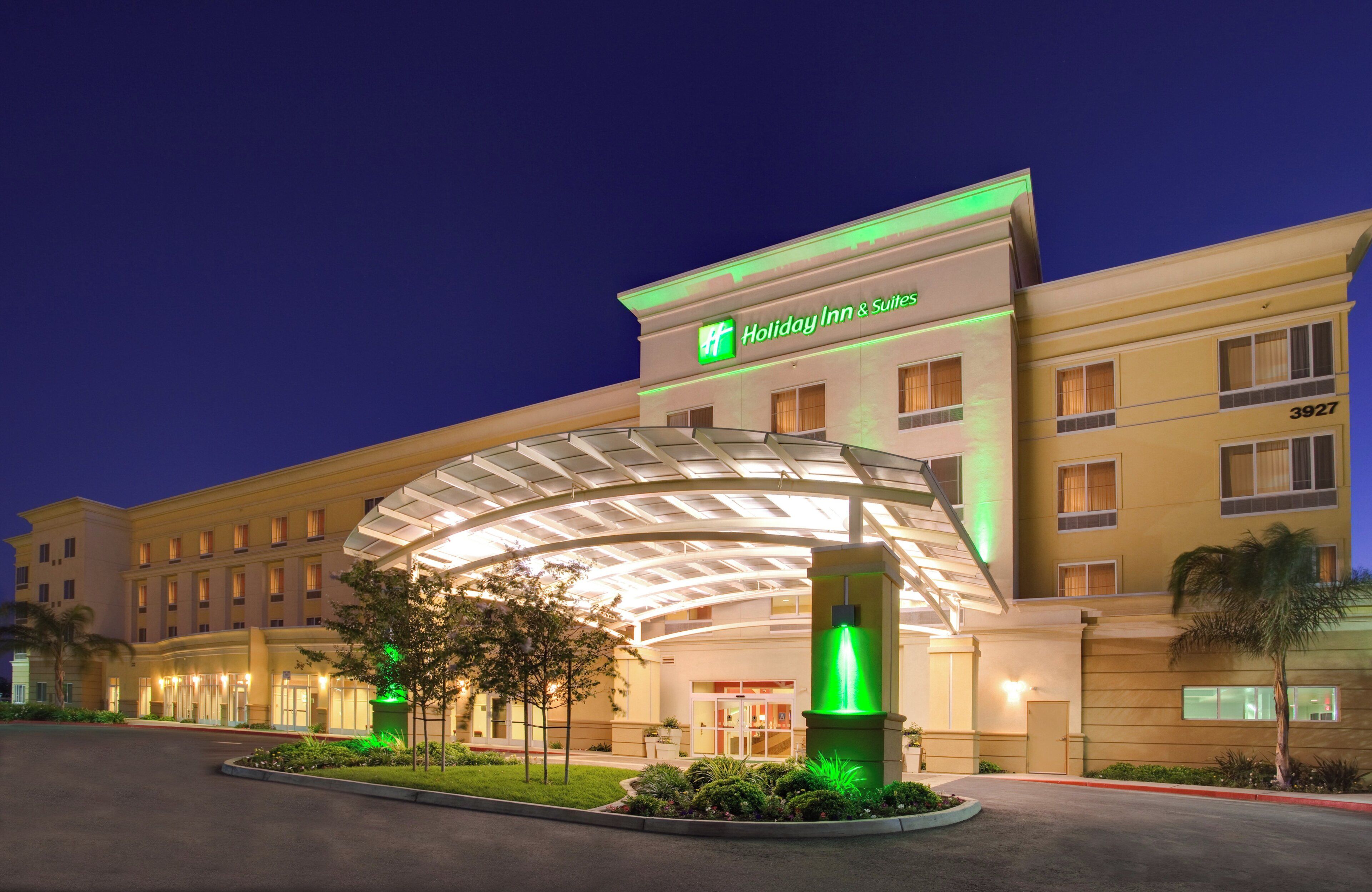 A Holiday Inn & Suites hotel with a covered entrance, multiple floors, and a well-lit facade.