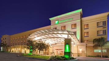 A Holiday Inn & Suites hotel with a covered entrance, multiple floors, and a well-lit facade.