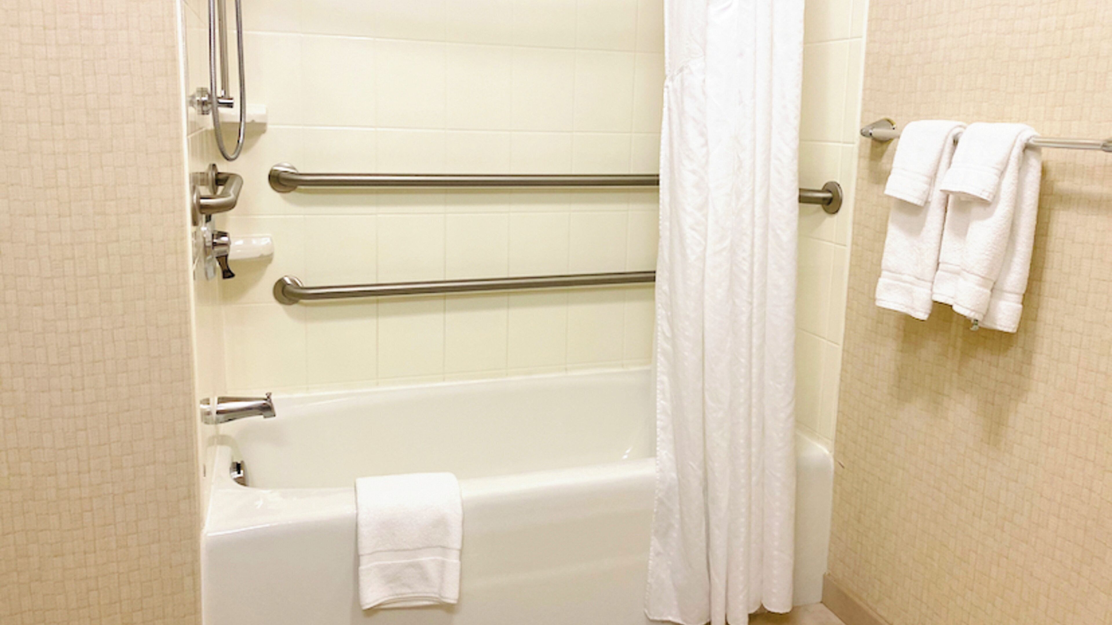 Une salle de bain standard équipée d’une baignoire, de barres d’appui, d’un rideau de douche et d’un porte-serviettes avec des serviettes.