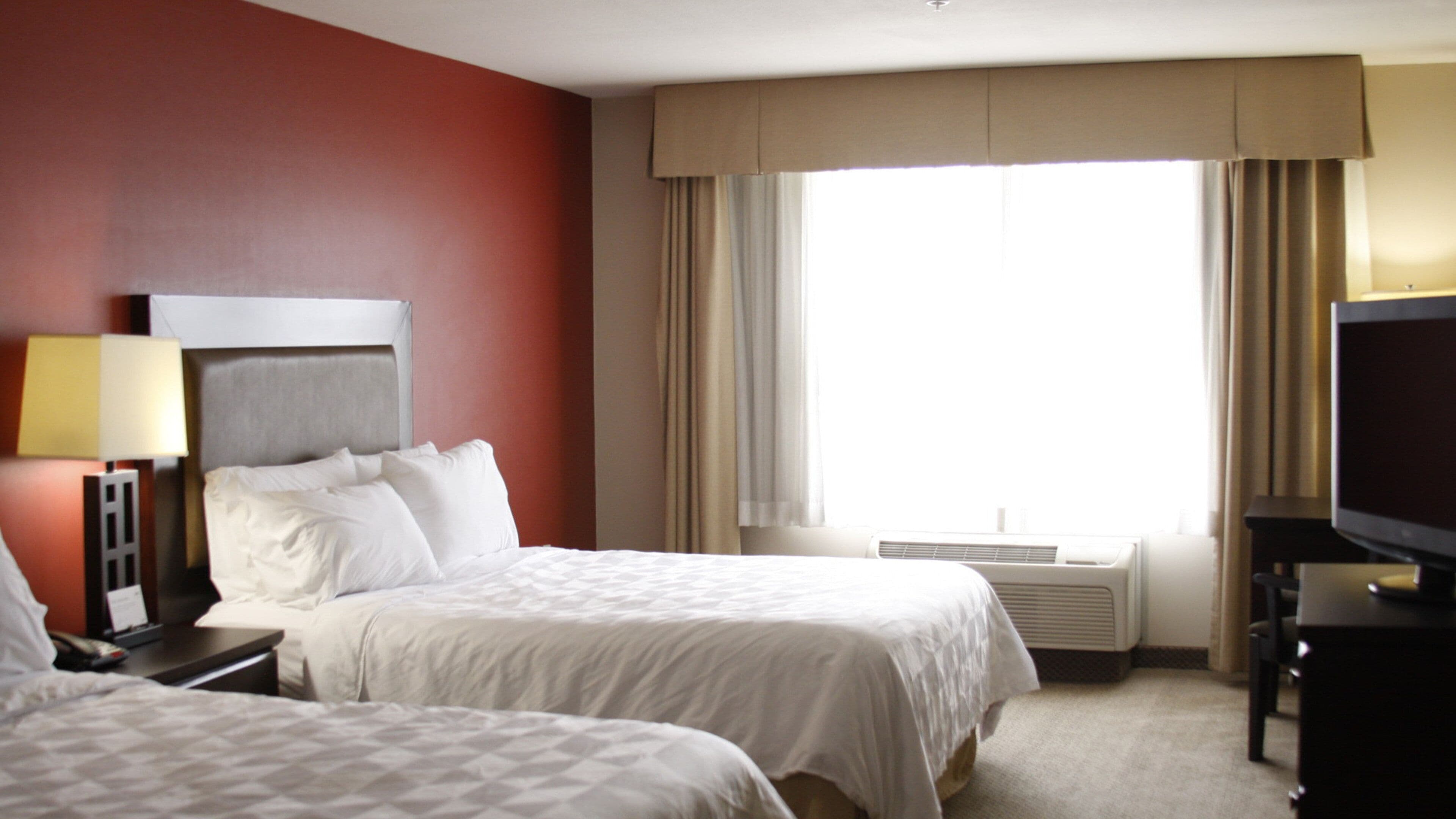 Quarto de hotel com duas camas, televisão, ar condicionado e janela com cortinas.