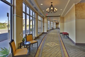 A hotel corridor with large windows, a patterned carpet, and a bench. - Holiday Inn & Suites Bakersfield by IHG (Bakersfield)