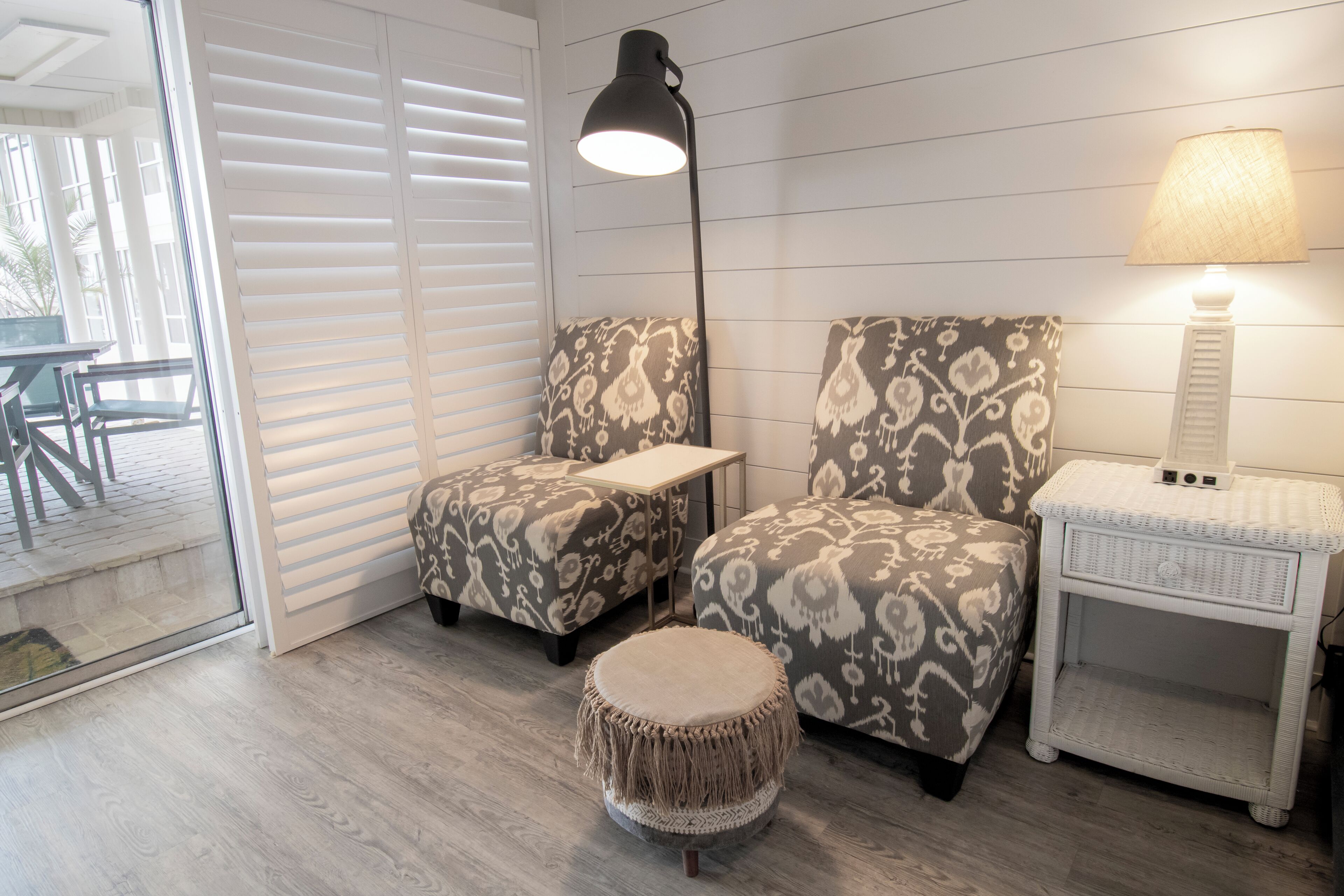 A room with patterned armchairs, a round ottoman, a side table, and a lamp.