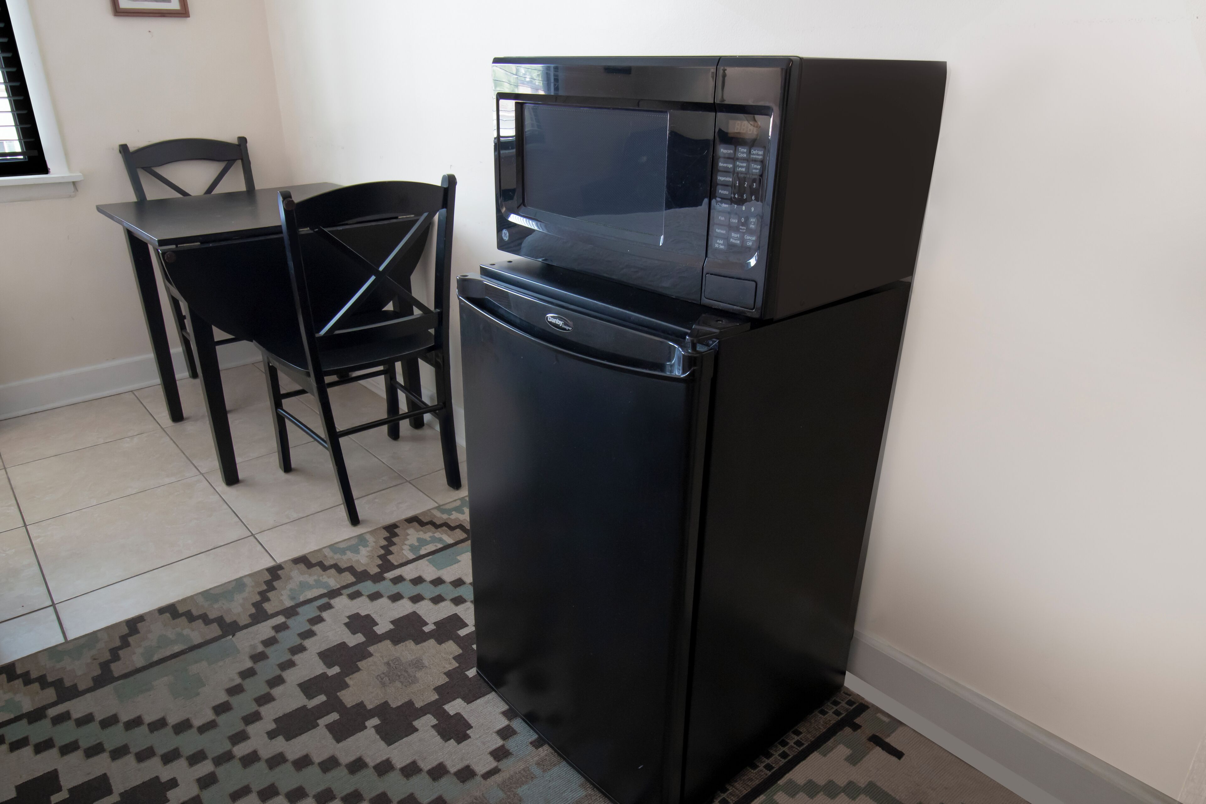 Una cucina compatta con un frigorifero e un forno a microonde neri, un tavolo da pranzo con sedie e un tappeto decorato.