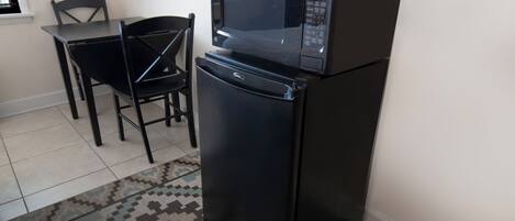 Una cucina compatta con un frigorifero e un forno a microonde neri, un tavolo da pranzo con sedie e un tappeto decorato.