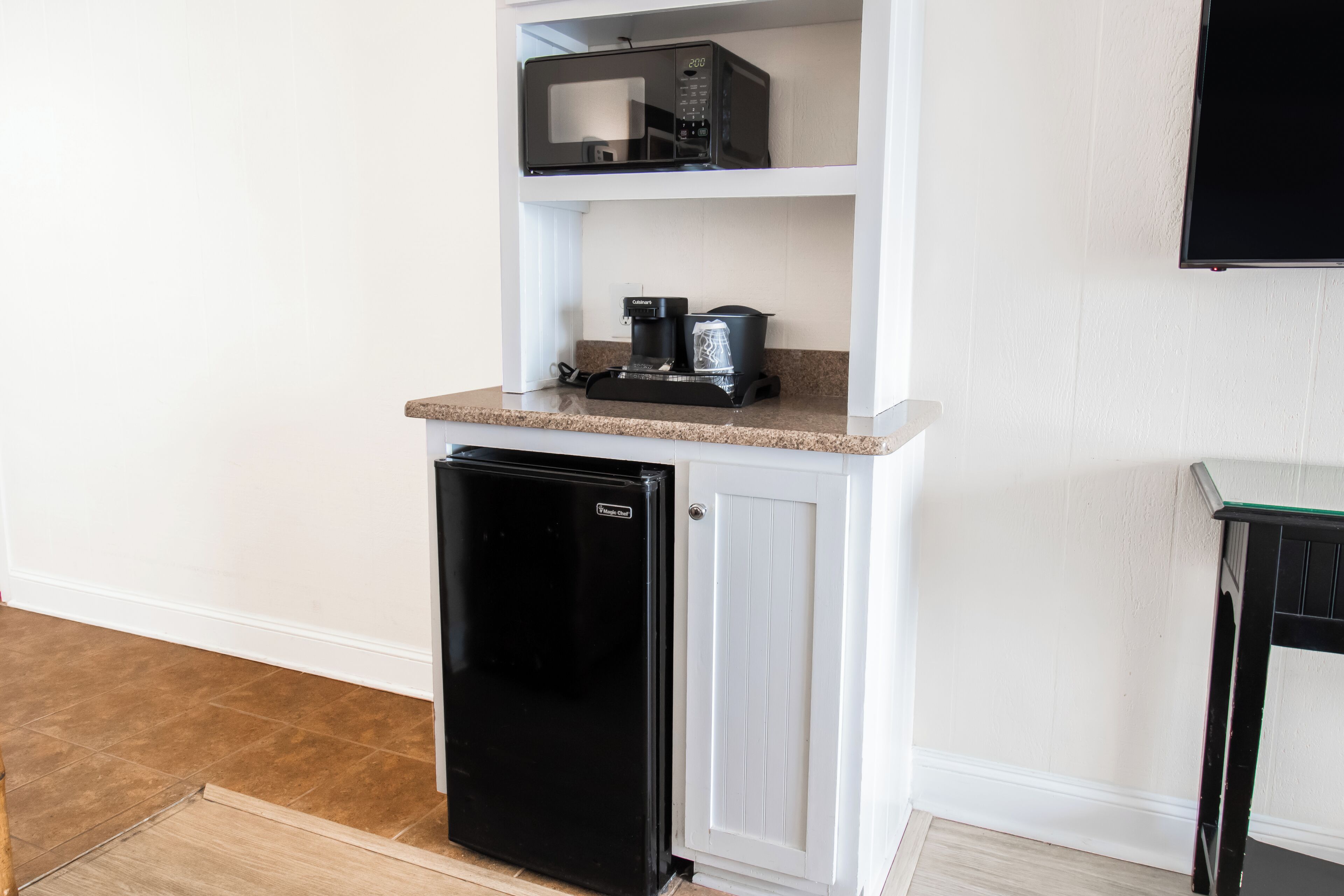 A compact kitchen with a refrigerator, coffee maker, and microwave on a white countertop.