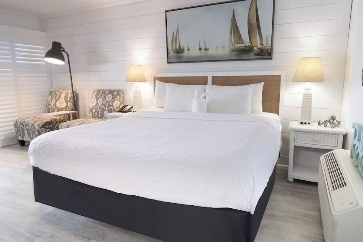 Quarto de hotel bem arrumado, com uma cama grande, duas mesas de cabeceira, uma cadeira e um quadro na parede.