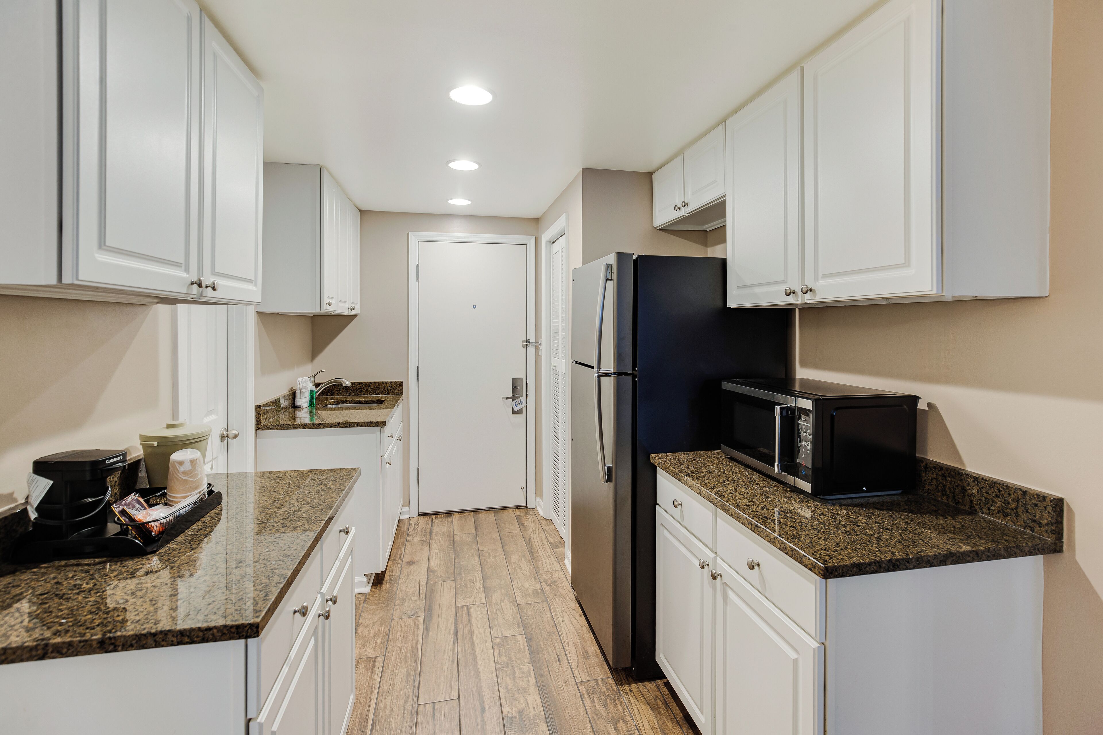 A compact kitchen with white cabinets, a black refrigerator, a microwave, and a coffee maker on the counter.