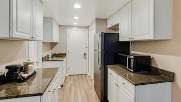 A compact kitchen with white cabinets, a black refrigerator, a microwave, and a coffee maker on the counter.