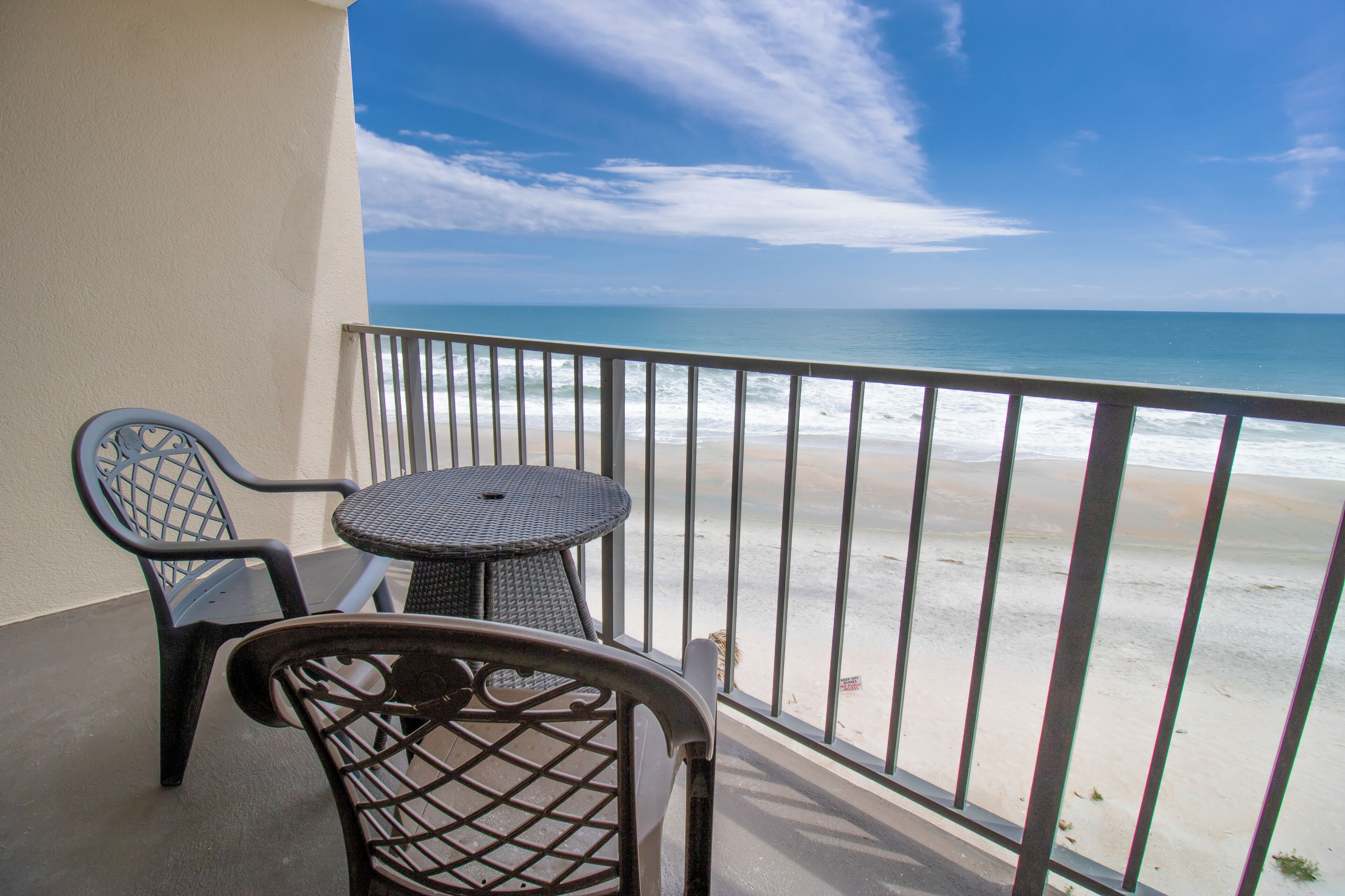 Un balcon avec vue sur la plage, comprenant une table ronde et deux chaises.