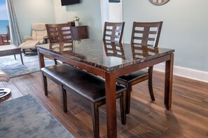 A dining area with a glass-top table, wooden chairs, and a bench. - The Oceanfront Litchfield Inn (Pawleys Island)