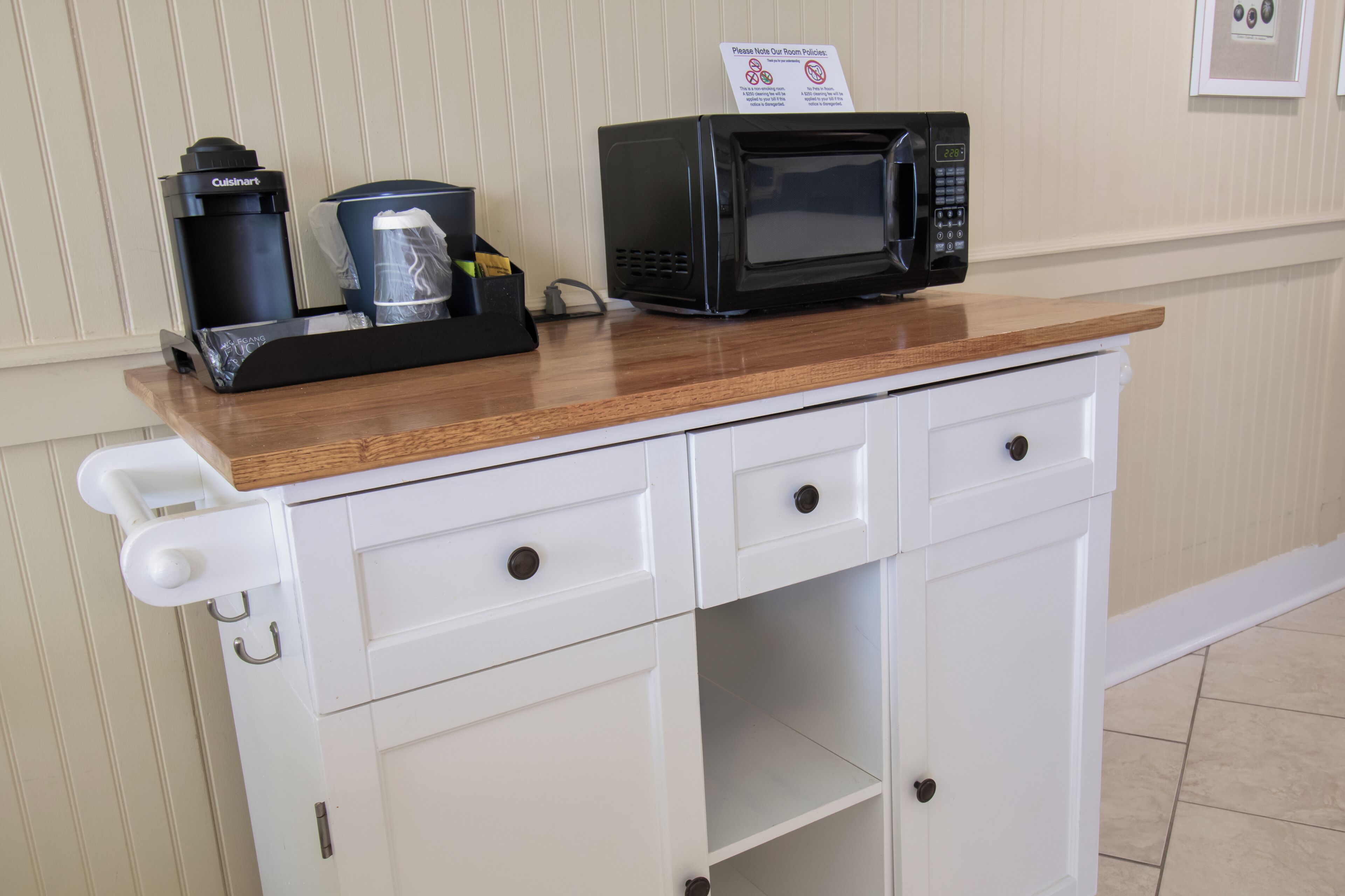 A kitchenette with a microwave, coffee maker, and a sign indicating room policies.