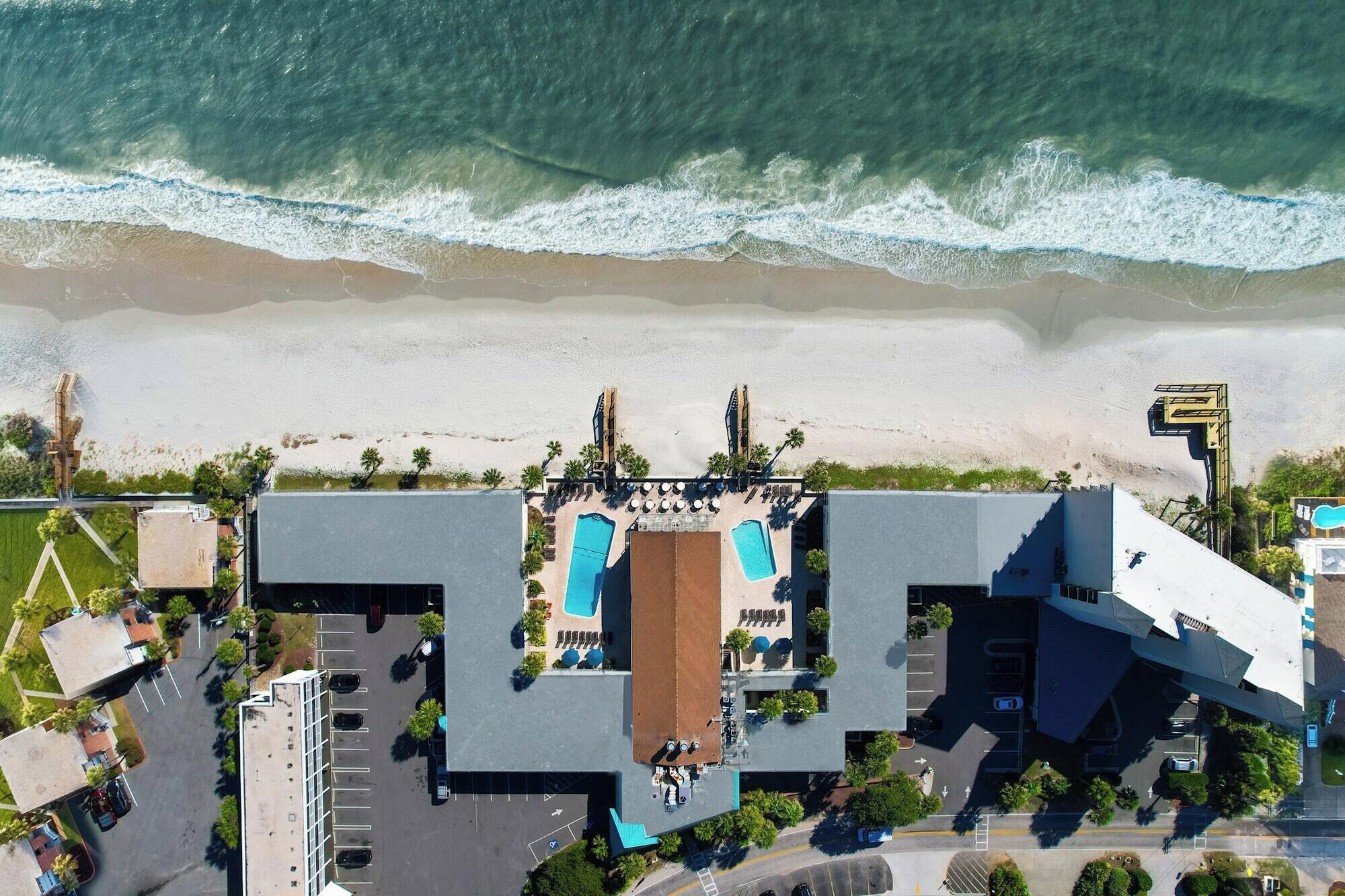 An aerial view of a resort with a pool, beach access, and a parking area.