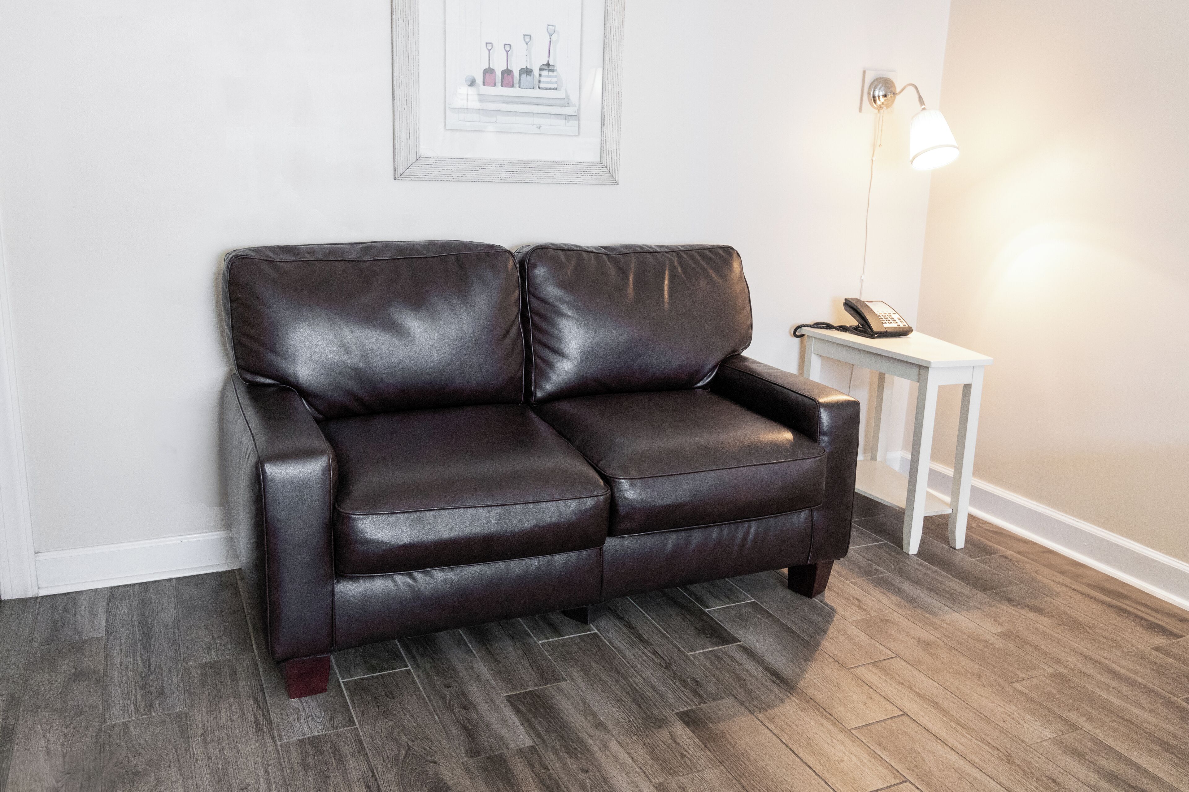 A dark brown leather sofa in a room with a white wall and a framed picture above it.