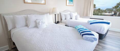 A hotel room with two beds, a large window with a view, and artwork on the walls.