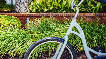 A bicycle with a white frame and black tires parked in front of a garden with green plants and a brick wall.
