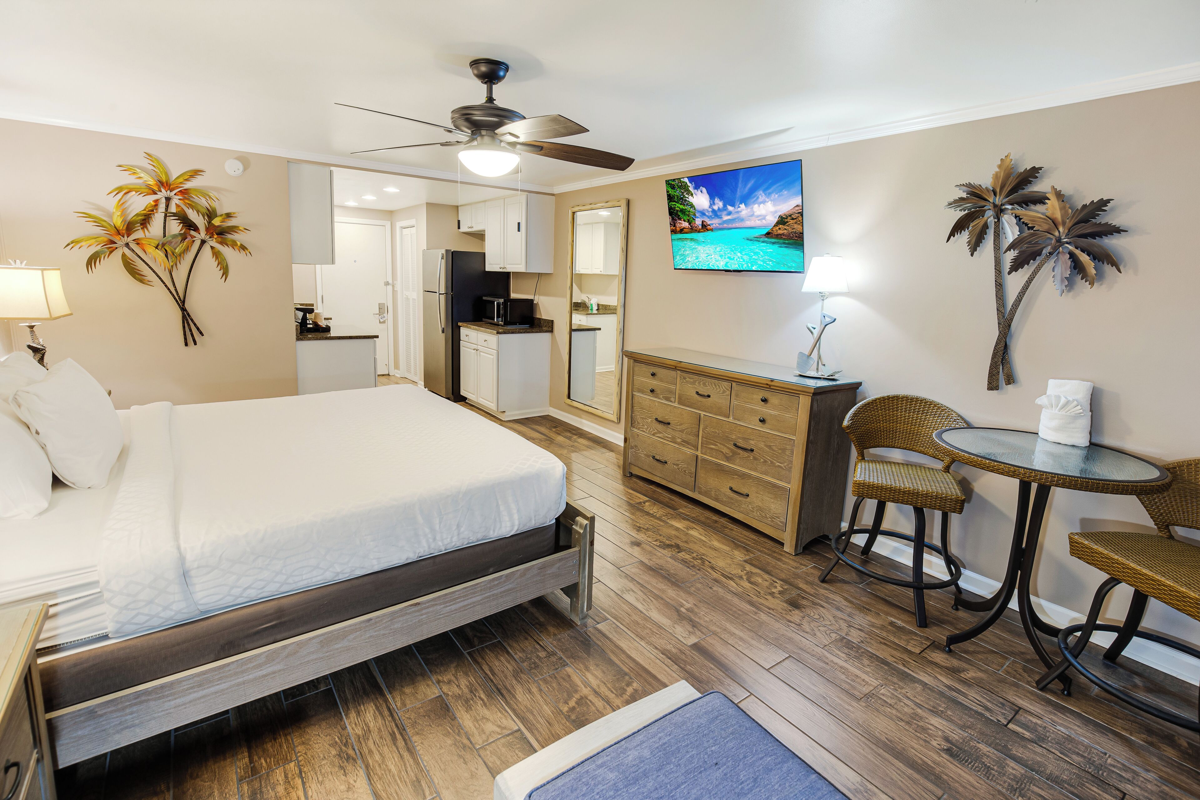 Une chambre d’hôtel équipée d’un lit, d’un bureau, d’une chaise, d’une petite table, d’un ventilateur de plafond et d’une télévision.