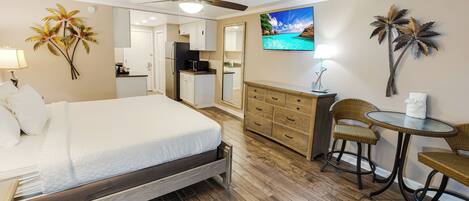 A hotel room with a bed, a desk, a chair, a small table, a ceiling fan, and a TV.