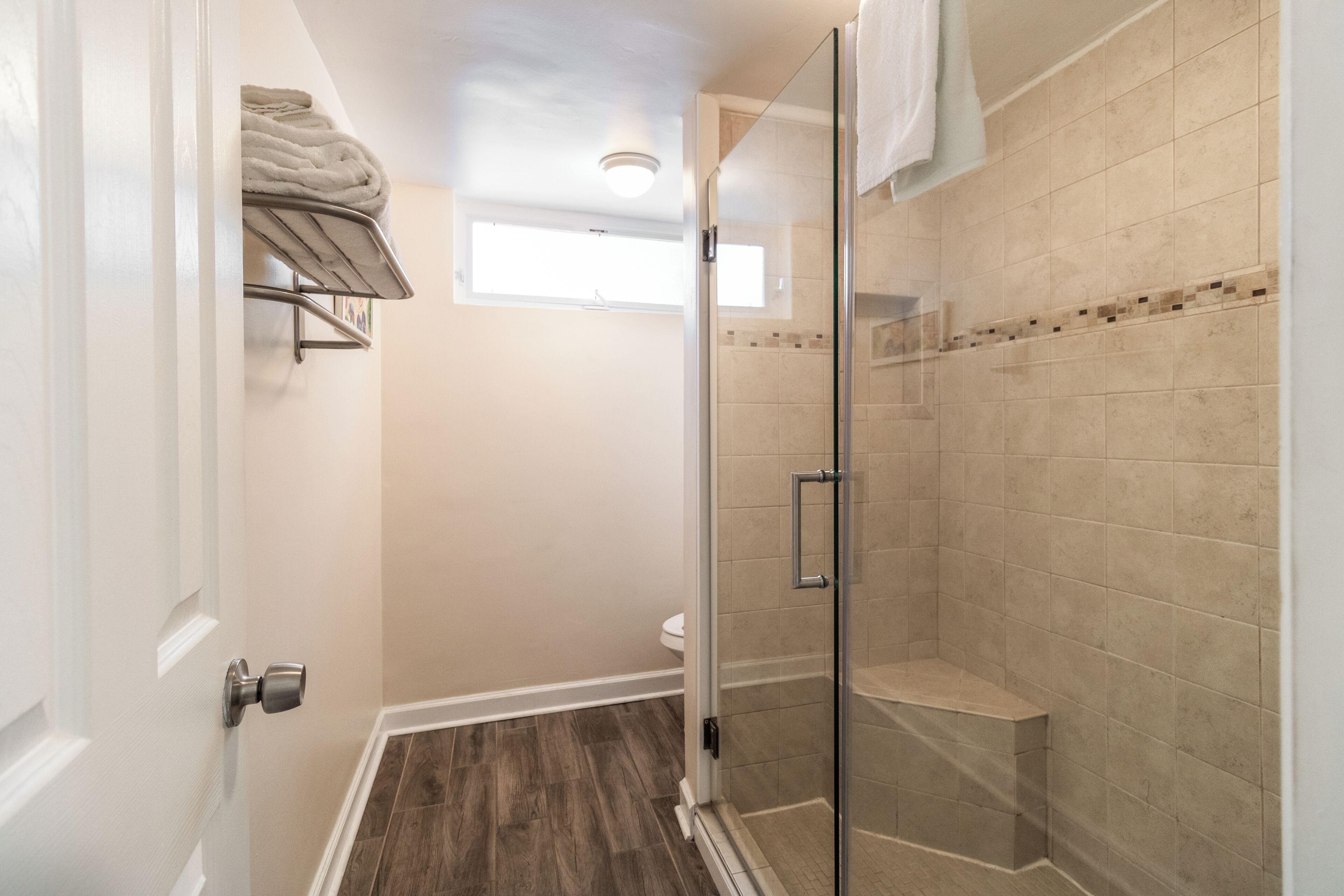 A bathroom with a glass shower enclosure, a toilet, and a shelf with towels.
