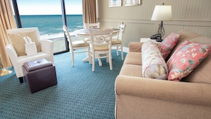 A room with a view of the ocean, a dining table with chairs, a sofa with floral cushions, and a lamp on a side table. - The Oceanfront Litchfield Inn (Pawleys Island)