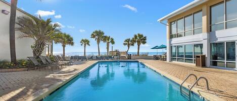 A swimming pool with lounge chairs, palm trees, and a building with large windows.