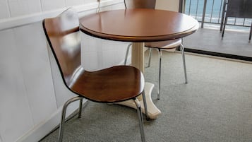 A round table with two chairs, a view of the ocean through a window, and a white wall.