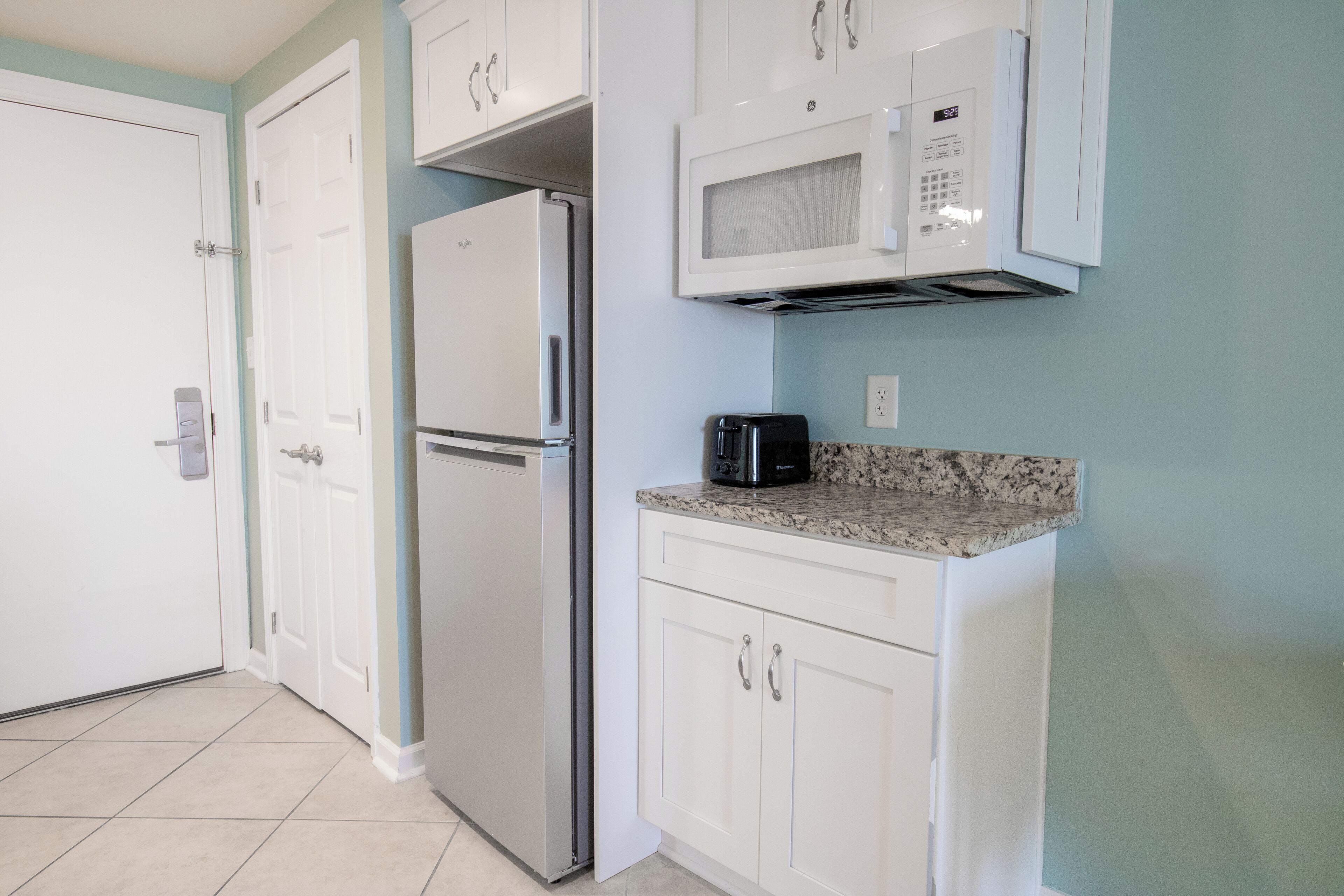 A kitchen with white cabinets, a stainless steel refrigerator, a microwave, and a granite countertop.