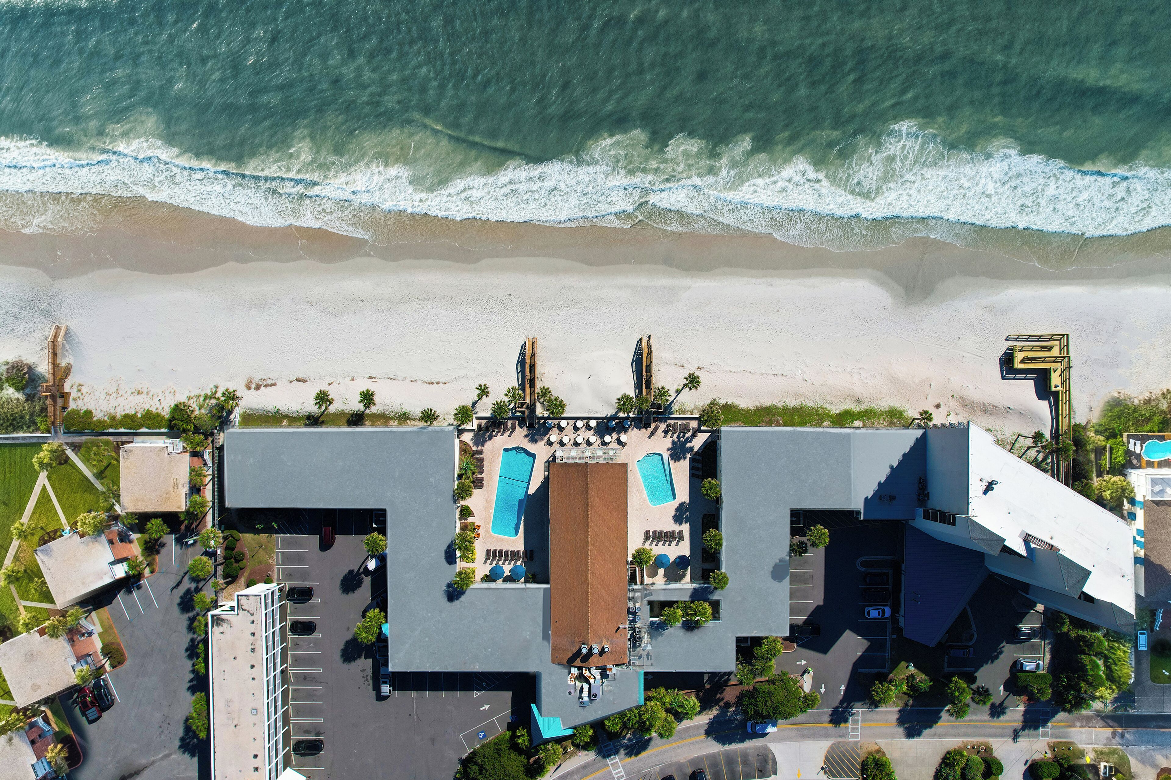 Vista aérea de un hotel con zona de piscina, aparcamiento y vistas a la playa.