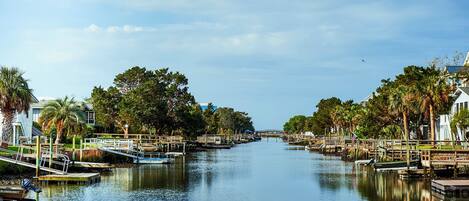 A calm river with boats docked on the sides, surrounded by trees and a bridge in the distance.