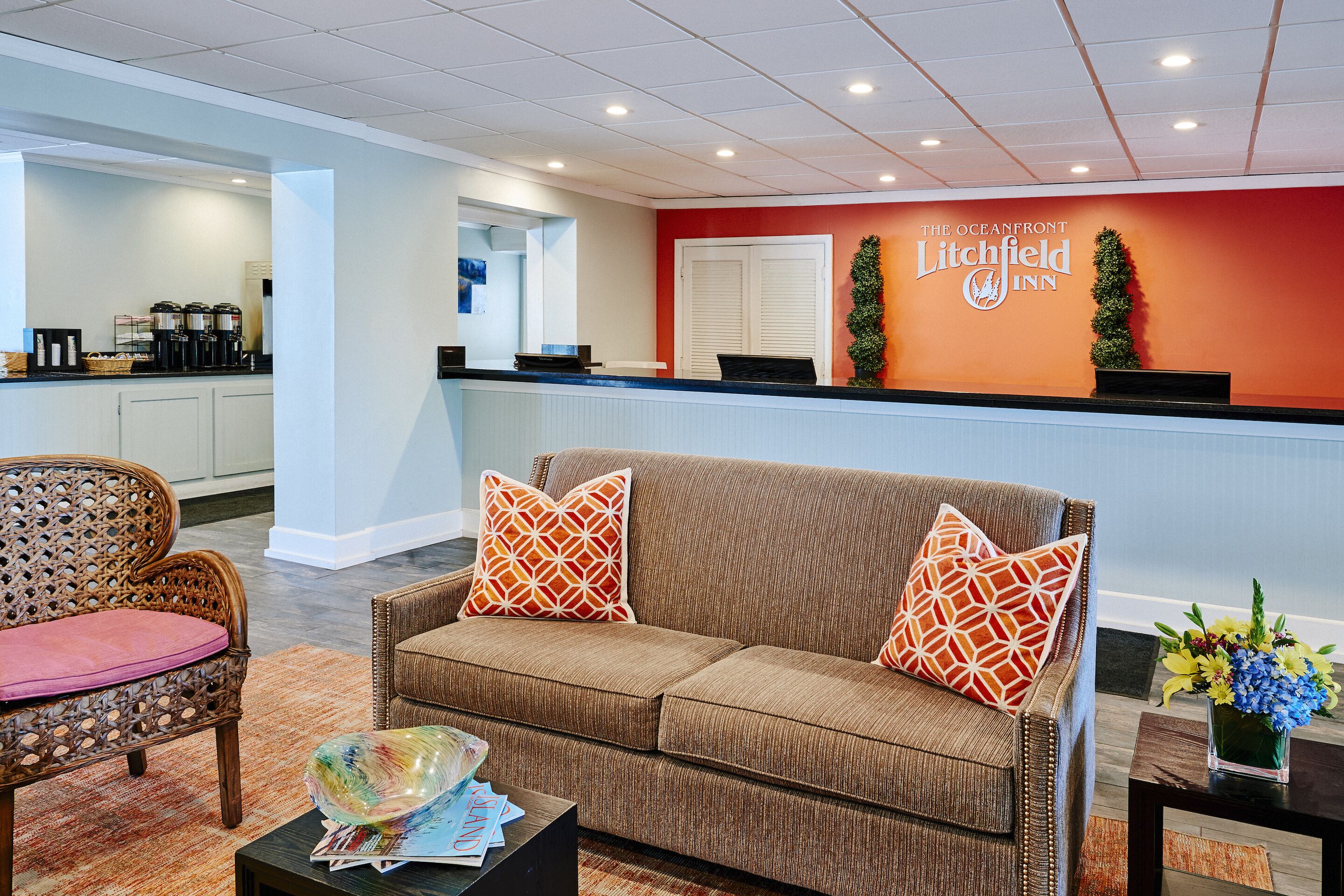 A reception area with a brown sofa, wicker chairs, a coffee station, and a reception desk.