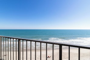 A beach view from a balcony with a railing, ocean, and clear sky. - The Oceanfront Litchfield Inn (Pawleys Island)