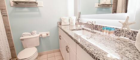A bathroom with a white toilet, a sink with a granite countertop, and a starfish decoration.