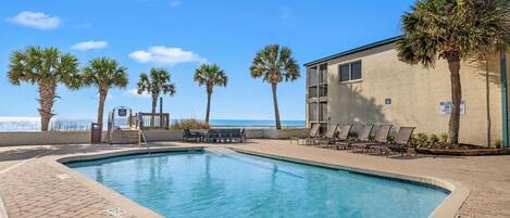 A swimming pool with lounge chairs, palm trees, and a building with a sign.
