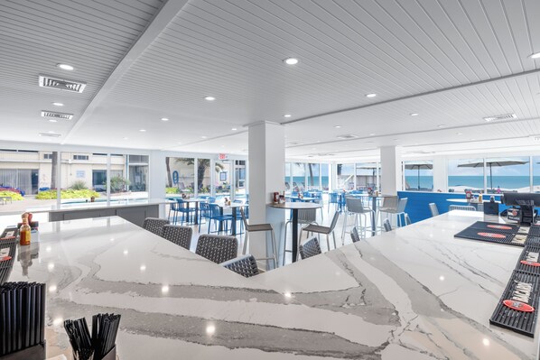 A modern bar area with a marble countertop, seating, and a view of the ocean. - The Oceanfront Litchfield Inn (Pawleys Island)