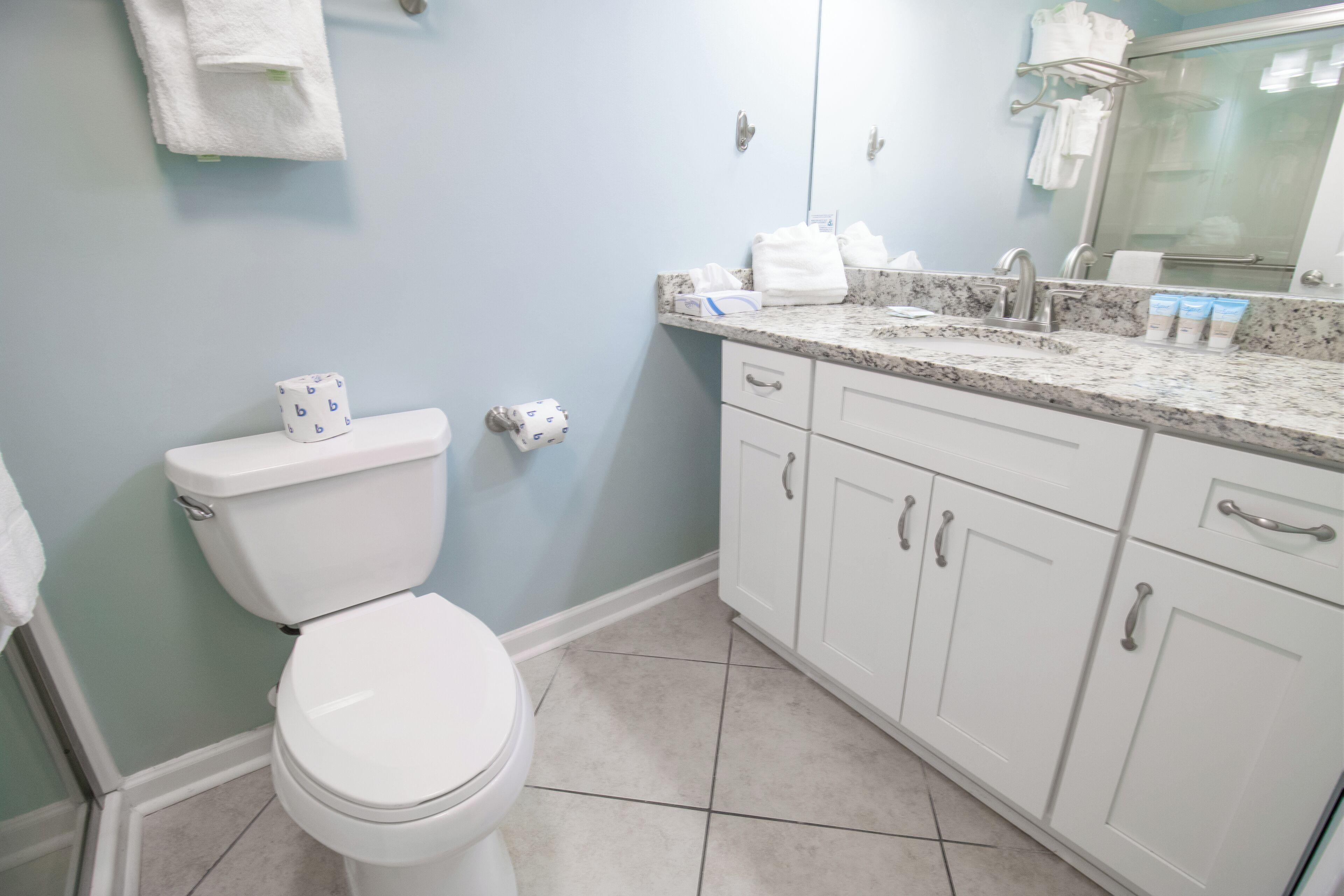 Une salle de bain avec des toilettes blanches, un lavabo doté d’un plan de travail en marbre et des meubles blancs.