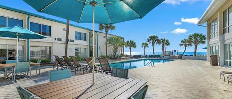 A poolside area with a wooden table, chairs, and a large umbrella.