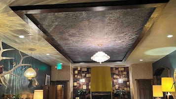 A spacious lobby with a high ceiling, a chandelier, and a fireplace. There are two sofas and a coffee table.