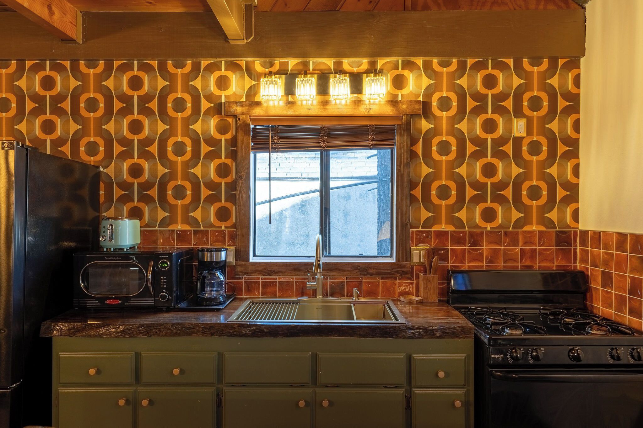 Una cocina con salpicadero estampado, una ventana con persianas, un fregadero, una estufa y un microondas.