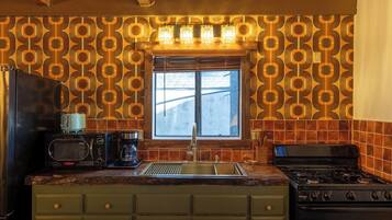 Una cocina con salpicadero estampado, una ventana con persianas, un fregadero, una estufa y un microondas.