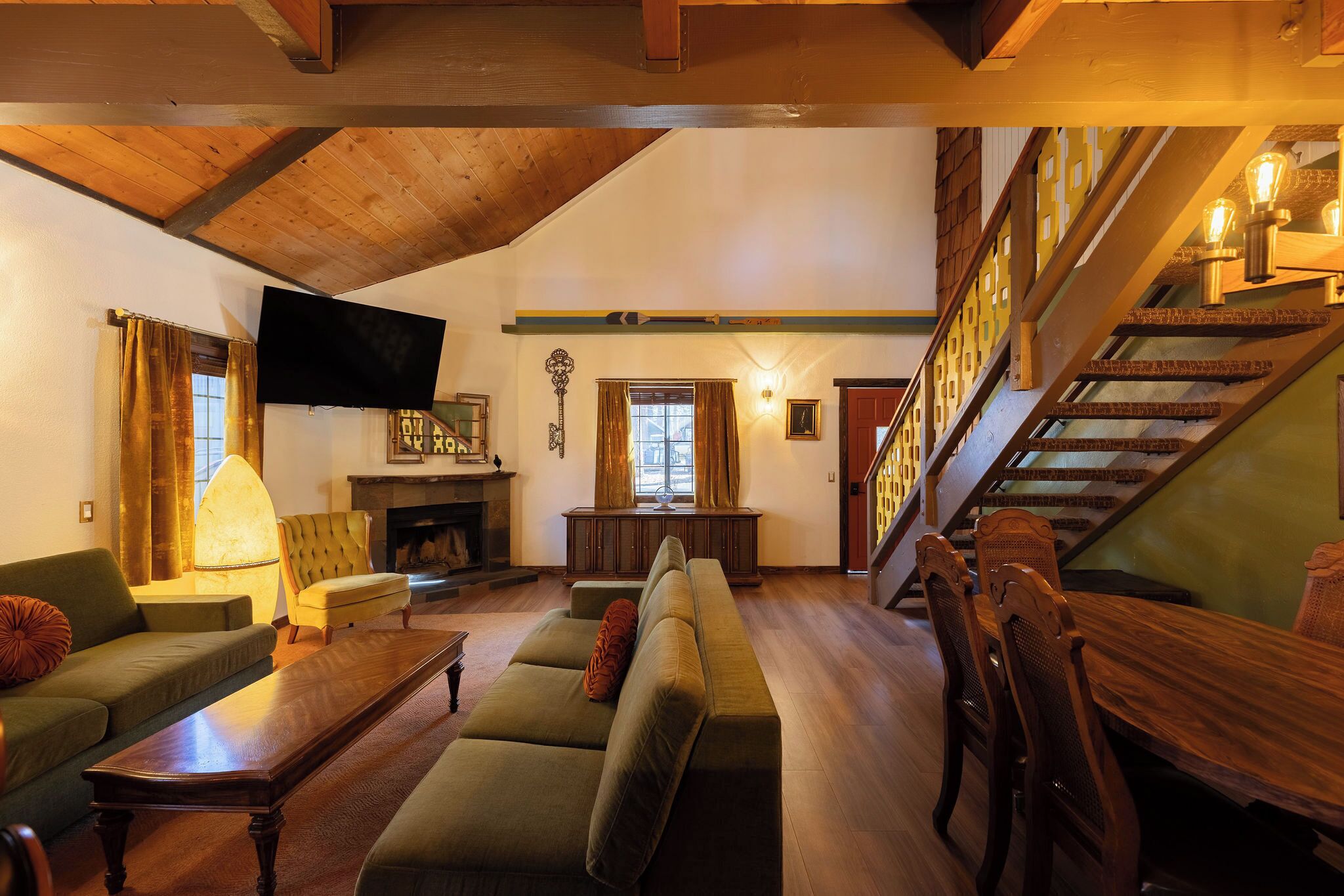 A spacious living room with a high ceiling, a fireplace, a staircase, and a dining area.