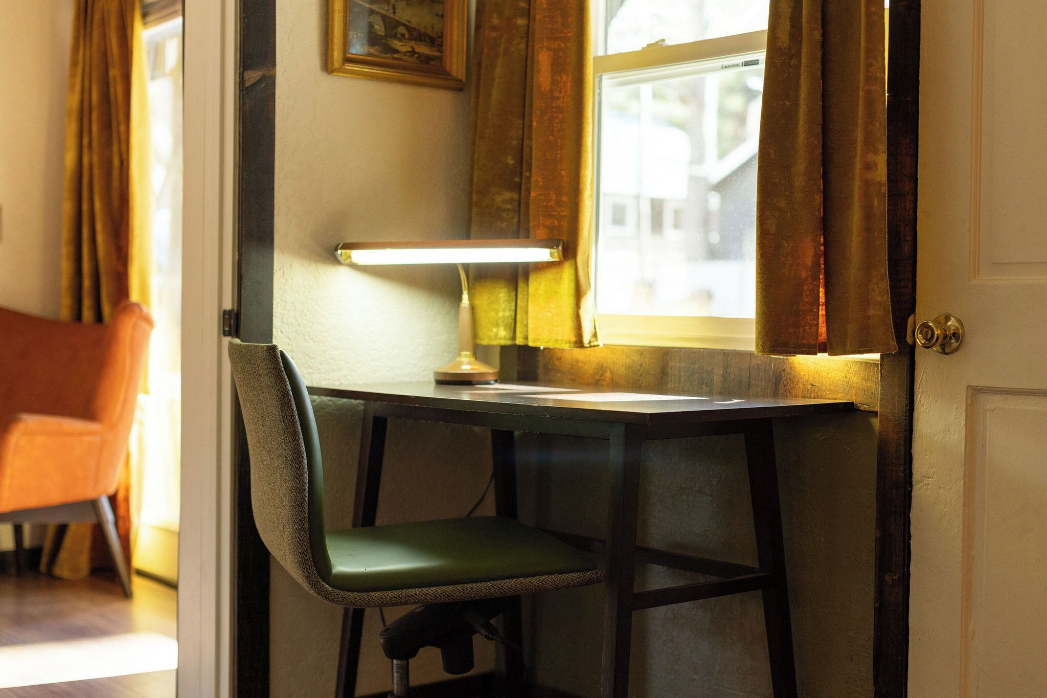Une pièce comprenant un bureau, une chaise, une lampe et une fenêtre avec des rideaux.
