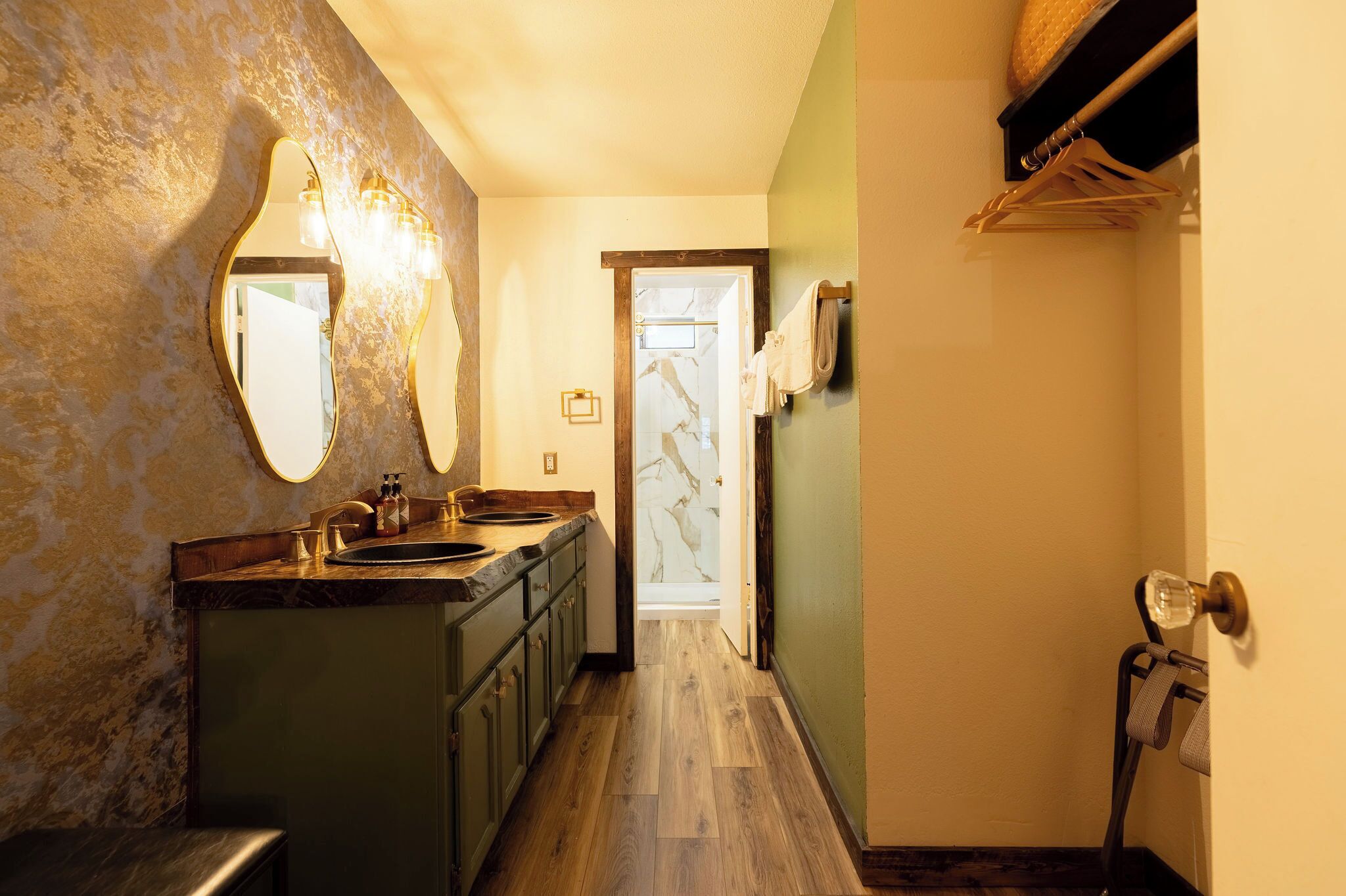 A narrow hallway with a wooden floor, a sink with a marble countertop, and a mirror with wall-mounted lights.
